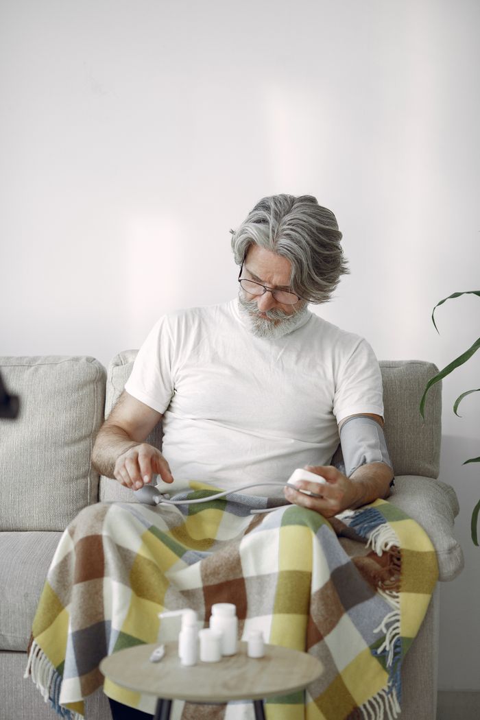 Mastering the First Impression: Your intriguing post title goes here Elderly man sitting on sofa with blanket, monitoring blood pressure with medication bottles.