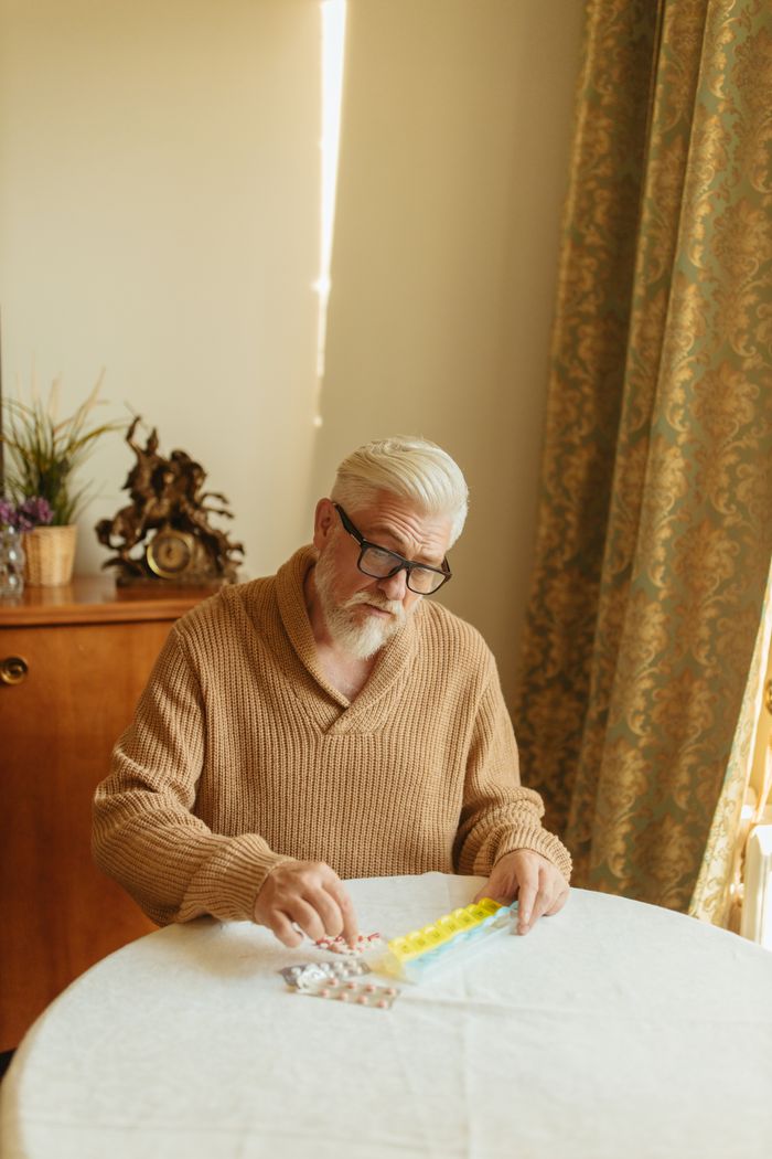 Elderly man with glasses arranging pills in a daily organizer at home.